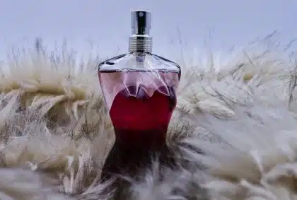 Anonieme handen met een parfumfles boven karamelkleurige stof en bloemen