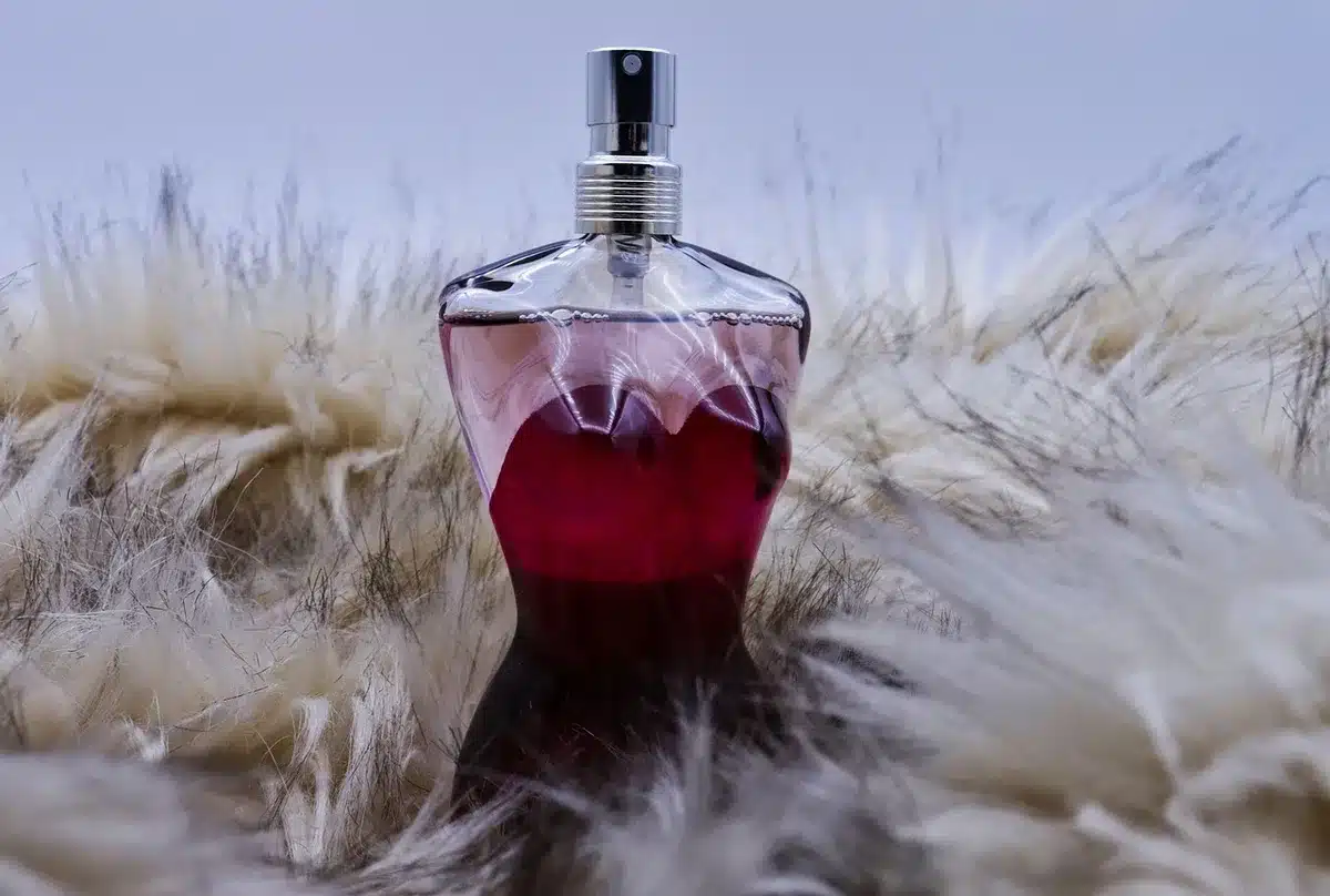 Anonieme handen met een parfumfles boven karamelkleurige stof en bloemen
